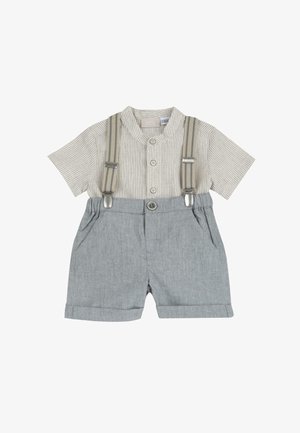 Chemise beige à rayures à manches courtes avec col montant, associée à un short gris clair maintenu par des bretelles beiges avec des attaches métalliques.
