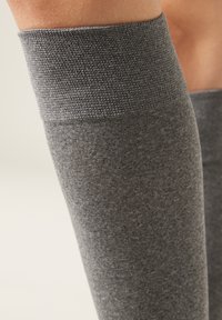Calcetines gris de hasta la rodilla con un tejido texturizado, que presentan una banda superior acanalada. El material parece suave y elástico para mayor comodidad.