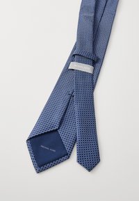 Cravatta blu con motivo geometrico, realizzata in tessuto. Presenta un'etichetta grigia con "MICHAEL KORS" e una texture liscia.