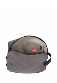 Grijze, zachte tas met een ronde vorm, bovenaan gesloten met een rits, en een beige interieur met een klein vakje en een merklabel.