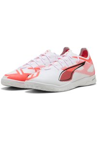 Chaussures de sport blanches avec une surface texturée, présentant des accents rouges et noirs, un design épuré et des semelles en caoutchouc non marquantes.