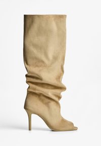 Vajaszínű, laza, térdig érő csizma, puha velúrból készült, peep-toe dizájnnal és magas stiletto sarkával. Sima textúra, finom Redők.