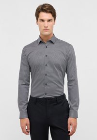 Camicia a maniche lunghe a fantasia bianca e nera, con colletto, chiusura a bottoni e vestibilità slim. Abbinata a pantaloni neri.