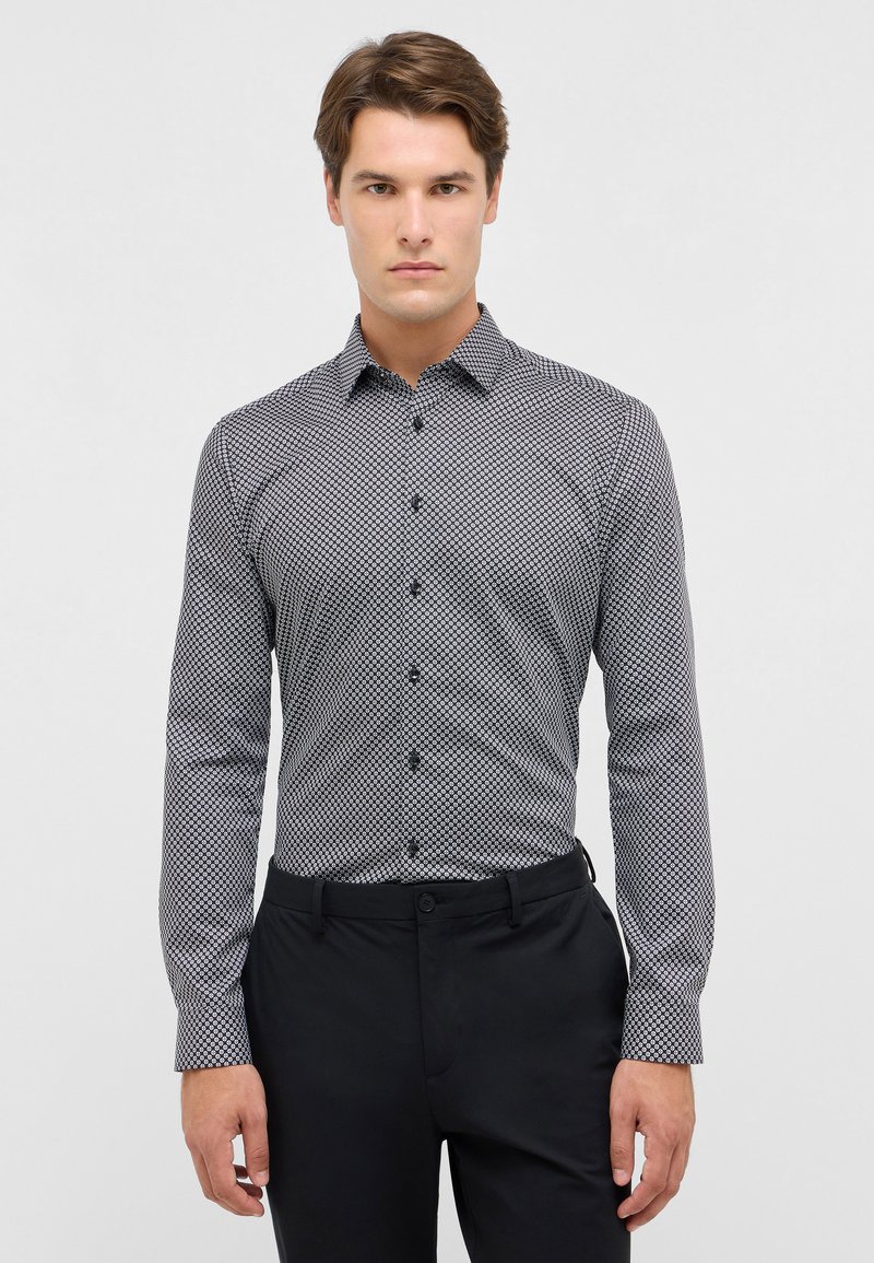 Camicia a maniche lunghe a fantasia bianca e nera, con colletto, chiusura a bottoni e vestibilità slim. Abbinata a pantaloni neri.