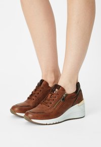 Baskets en cuir marron avec texture en mesh, fermeture à lacets et fermeture éclair latérale. Semelle compensée avec une base blanche et un détail accent doré.