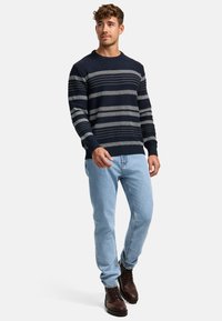 Marineblau gestreifter Pullover mit hellgrauen und weißen Streifen, mit gerippten Bündchen, kombiniert mit hellblauen Jeans und braunen Schnürstiefeln.
