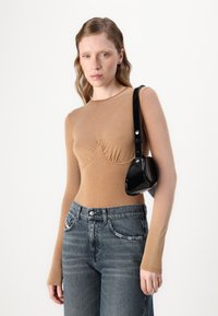 Langärmliges, hellbraunes Oberteil mit gerafften Details an der Brust, kombiniert mit hochgeschnittenen, dunkelblauen Jeans und einer kleinen schwarzen Schultertasche.