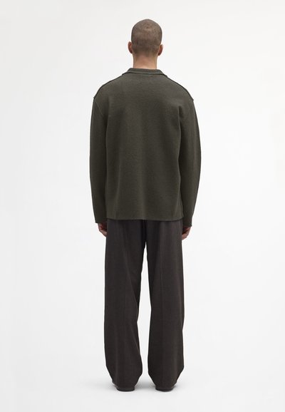 Olivgrünes Wollmischung Langarmhemd mit lockerer Passform, ausgestattet mit einem flachen Kragen und strukturierter Oberfläche, kombiniert mit dunklen, weiten Hosen.