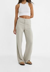 Lys grå, løstsiddende, åndbare bukser lavet af et glat materiale med elastisk talje og snor. Sæt sammen med en hvid crop top.