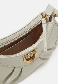 Borsa in pelle verde chiaro con un design a pieghe, hardware in tonalità oro e chiusura con zip. L'interno presenta foderatura marrone e dettaglio del logo del marchio.