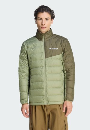 Man wearing olive green Terrex puffer jacket with front zipper and brown multi-pocket pants, standing against light background.