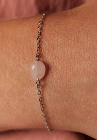 Rozenkwarts kralenarmband met een zilveren metalen ketting, met een gladde, ronde roze edelsteen in het midden tegen de huidtextuur.