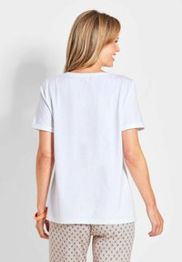 Witte katoenen T-shirt met korte mouwen en een ronde halslijn. De achterkant heeft een relaxte pasvorm. Gepaarde met een gestreepte pyjamabroek.