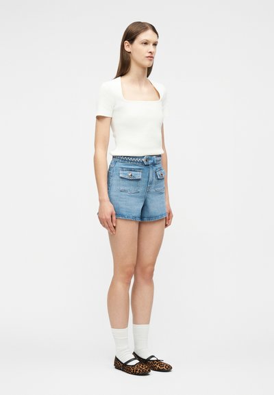 Γυναίκα που φοράει λευκό τοπ με κοντά μανίκια και τετράγωνη λαιμόκοψη, ψηλόμεσα τζιν σορτς με εμπρόσθιες τσέπες, λευκές κάλτσες και φλατ παπούτσια με τύπωμα λεοπάρδαλης.