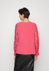 Top fúcsia com mangas longas de renda transparente, decote redondo e um corte solto, combinado com uma saia de couro preta. Tecido texturizado por toda a peça.