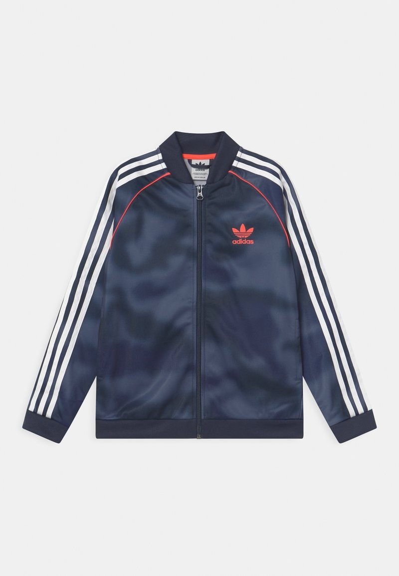 Veste de sport en satin bleu marine avec des accents blancs et rouges, trois bandes blanches sur les manches et fermeture éclair à l'avant. Présente un logo sur la poitrine.