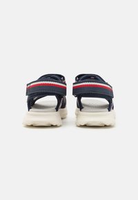 Navy sport sandals with adjustable straps, red and white accents, and cushioned white rubber soles. Rear view displays padding and texture details.