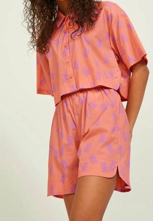 Woman wearing a loose, short-sleeve, button-up coral shirt and matching shorts with purple floral print.