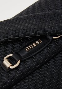 Borsa a tracolla nera intrecciata con una superficie liscia, dotata di una chiusura in metallo dorato e di un'etichetta in pelle nera con la scritta "GUESS" in rilievo.