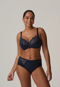 Navy blue biustonosz i komplet majtek o wysokim stanie z koronkowymi detalami i kwiatowymi wzorami. Posiada regulowane ramiączka i gładką teksturę.