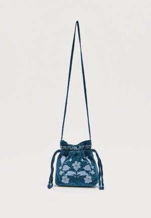 Türkiisroheline tõmbenööriga õlakott pika rihmaga ja helesinise lilleliste tikanditega esiküljel, taustaks tavaline pind.