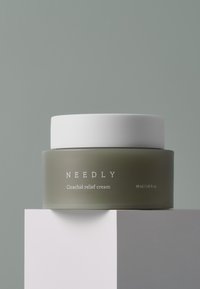 Crema de alivio Cicachid en un frasco corto, redondeado, mate de color verde oliva con una tapa blanca lisa; presenta texto blanco en el frasco.