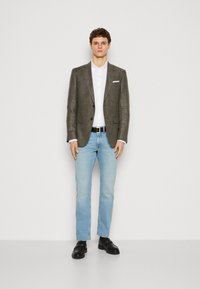 Blazer texturat gri peste o cămașă albă, blugi albaștri deschisi și mocasini negri cu accente aurii. Design simplu, modern, fără modele suplimentare.
