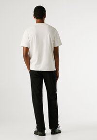 Hele halli lühikeste varrukatega t-särk, millel on mugav lõige, kombineeritud mustade pükste ja mustade lukkudega kingadega, vaadatuna tagant.