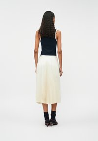 Top fără mâneci de culoare bleumarin asociat cu o fustă midi plisată de culoare crem. Șosete și pantofi cu toc completează ținuta. Accent pe texturi și design stratificat.