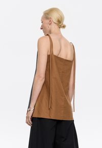 Canotta in lino marrone con spalline sottili e vestibilità comoda. Presenta una schiena scoperta e una texture sottile, abbinata a pantaloni larghi neri.