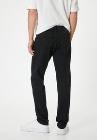 Vaqueros de mezclilla negra con corte recto, cinco bolsillos y detalles de costura sutil, combinados con zapatillas blancas y una camisa de manga corta.