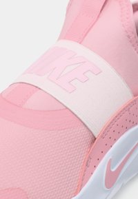 Różowe slip-on sneakersy Nike, charakteryzujące się fakturowaną cholewką, elastycznym paskiem z logo oraz białą podeszwą z różowymi akcentami.