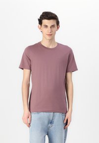 Kortermet t-skjorte med rund hals i mauve, laget av myk bomull. Har en subtil logo på brystet og en avslappet passform. Brukt sammen med lyseblå jeans.