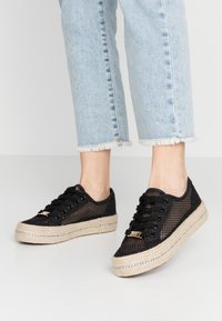 Sneaker nere in rete con una piattaforma in juta, caratterizzate da un upper testurizzato e dettagli in hardware dorato. Indossate con jeans azzurri sfilacciati.