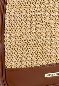 Textura de paja trenzada en un beige natural con acentos de cuero marrón. Presenta una placa de logo metálica, que muestra patrones de tejido intrincados.