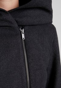 Giacca con cappuccio grigio scuro, con chiusura a zip, caratterizzata da una morbida texture in feltro e un ampio colletto ripiegato. Dettagli di chiusura lampo in metallo sono visibili.