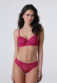 Reggiseno in pizzo fucsia con coppe rigide e spalline regolabili, abbinato a mutandine a vita alta con bordi scallop e motivo floreale.