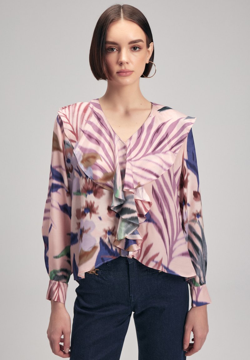 Blouse florale avec col et manches volantés dans des teintes de rose, bleu et vert. Tissu doux et léger avec une coupe décontractée.