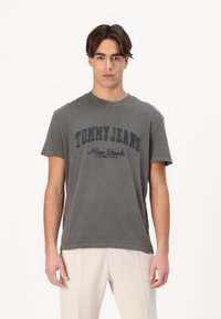 Camiseta de algodón gris con el texto "TOMMY JEANS New York" en un contraste azul oscuro. Cuello redondo y mangas cortas.