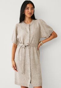 Beige gebreide jurk met korte pofmouwen, ronde hals, knopen aan de voorkant en een bijpassende riem. Zachte textuur met ribbelboorddetails.