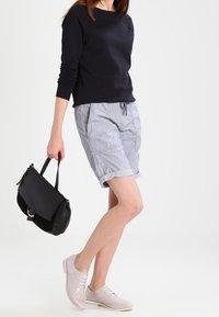 Pull noir à manches longues, short rayé gris et chaussures oxford rose clair. Sac à main noir avec une bandoulière longue et des accessoires dorés.