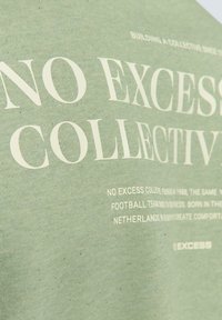 Groene katoenen T-shirt met grote witte tekst en branding, inclusief extra details. Zachte textuur met een ontspannen pasvorm.