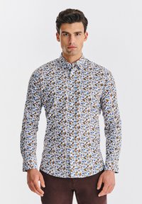 Koszula na długi rękaw z guzikami na białym tle, zdobiona kwiatowym wzorem w odcieniach niebieskiego i brązowego. Kołnierzyk, dopasowany krój.