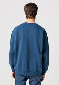Sweat-shirt bleu à col rond en tissu doux, avec une coupe décontractée, des poignets côtelés et un col cousu. Vue arrière montrée.