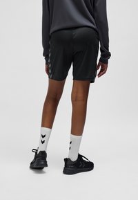 Zwarte atletische shorts met een gladde textuur, voorzien van zijaccenten. Paar witte sokken met zwarte chevronpatronen en zwarte hardloopschoenen.