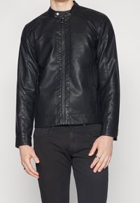 Veste en cuir noir avec un col haut, fermeture éclair à l'avant et deux poches latérales. Présente une texture lisse et un design ajusté.