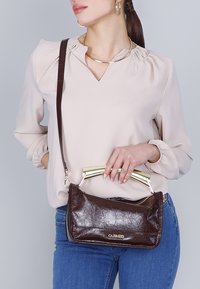 Brun läderhandväska med guldfärgad detaljer, rektangulär form, slät textur och avtagbar axelrem. Har en dragkedjestängning.