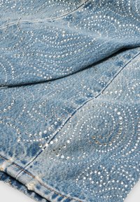 Lichtblauwe denimstof met zilveren rhinestenenpatronen die draaiende en paisley-achtige ontwerpen vormen, zichtbare stiksels en licht uitgerafelde randen.
