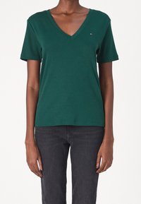 Grön bomullst-shirt med kort ärm och V-ringning som har en liten logotyp på vänster bröst och en klassisk passform. Slät textur och enkelt design.