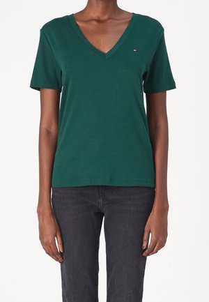 Camiseta verde de algodón de manga corta y cuello en V con un pequeño logo en el lado izquierdo del pecho y un corte clásico. Textura suave y diseño sencillo.